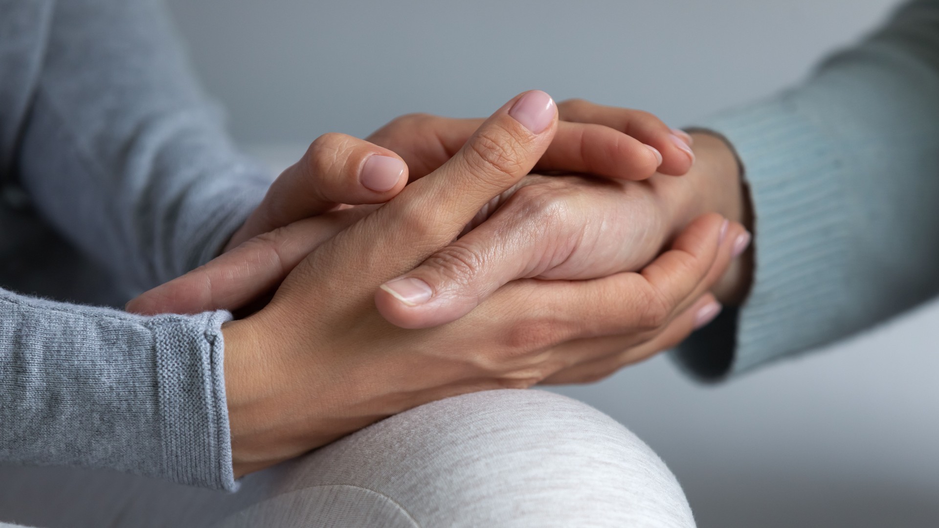 Close up young daughter comforting, holding mature mother hand