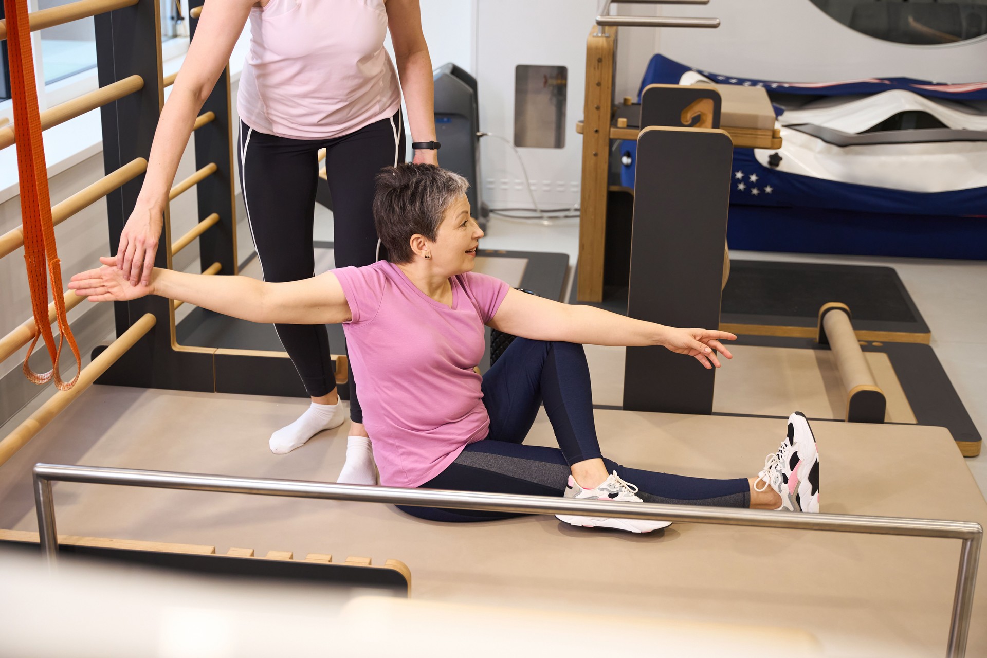 Partial female trainer helping smiling middle aged caucasian woman stretching